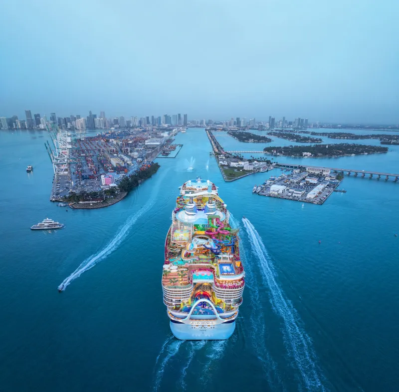 Icon of the Seas arriving in Miami Harbor with cityscape in background, aerial view.