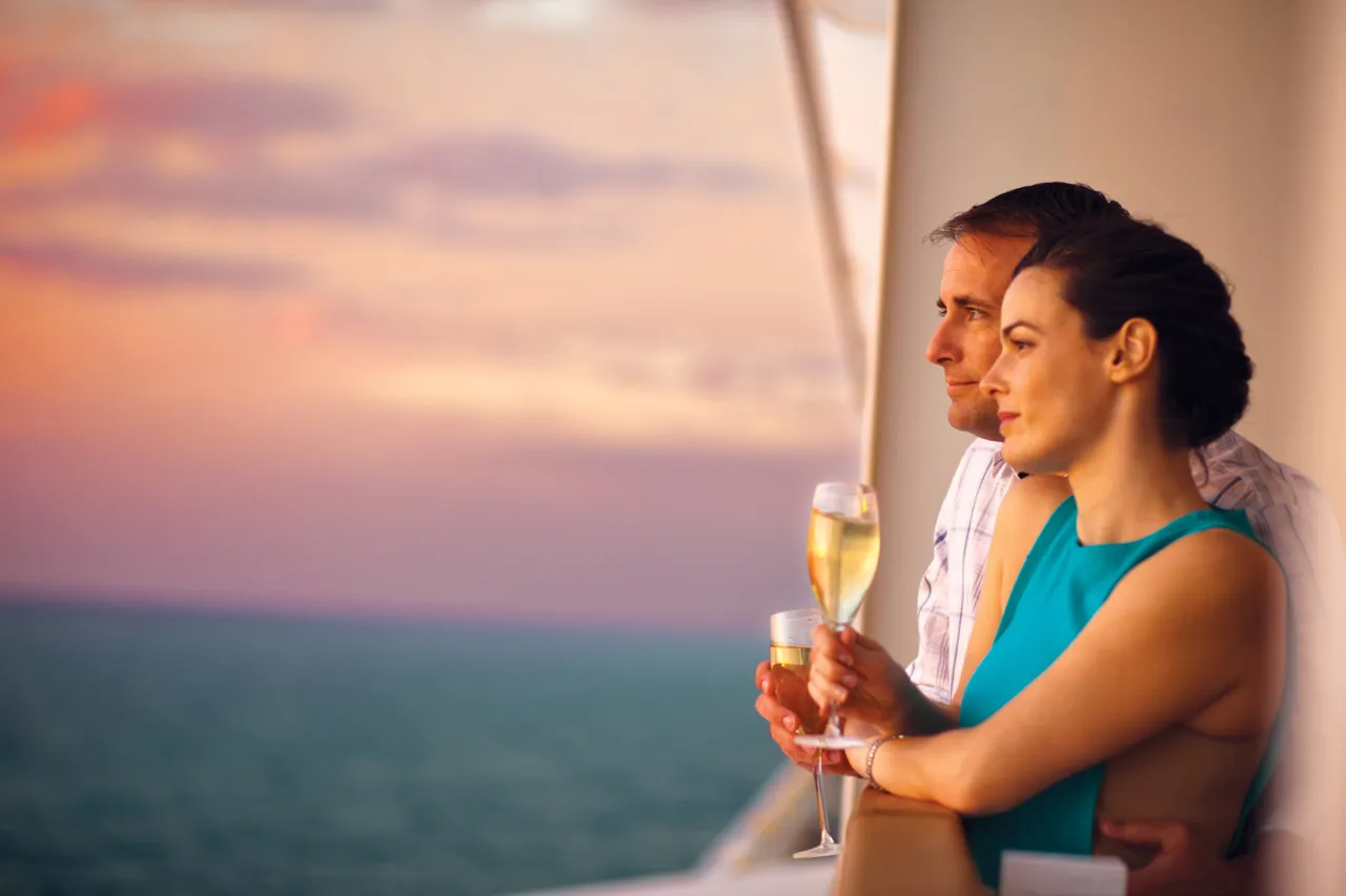 Couple standing at ship railing during golden sunset with ocean horizon backdrop