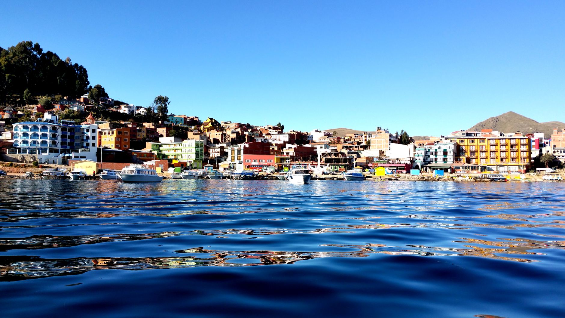 Colorful waterfront buildings of Copacabana town rising along the shoreline with boats anchored on the water, evoking the vibrant Caribbean port atmosphere of South American cruise destinations like Cartagena.