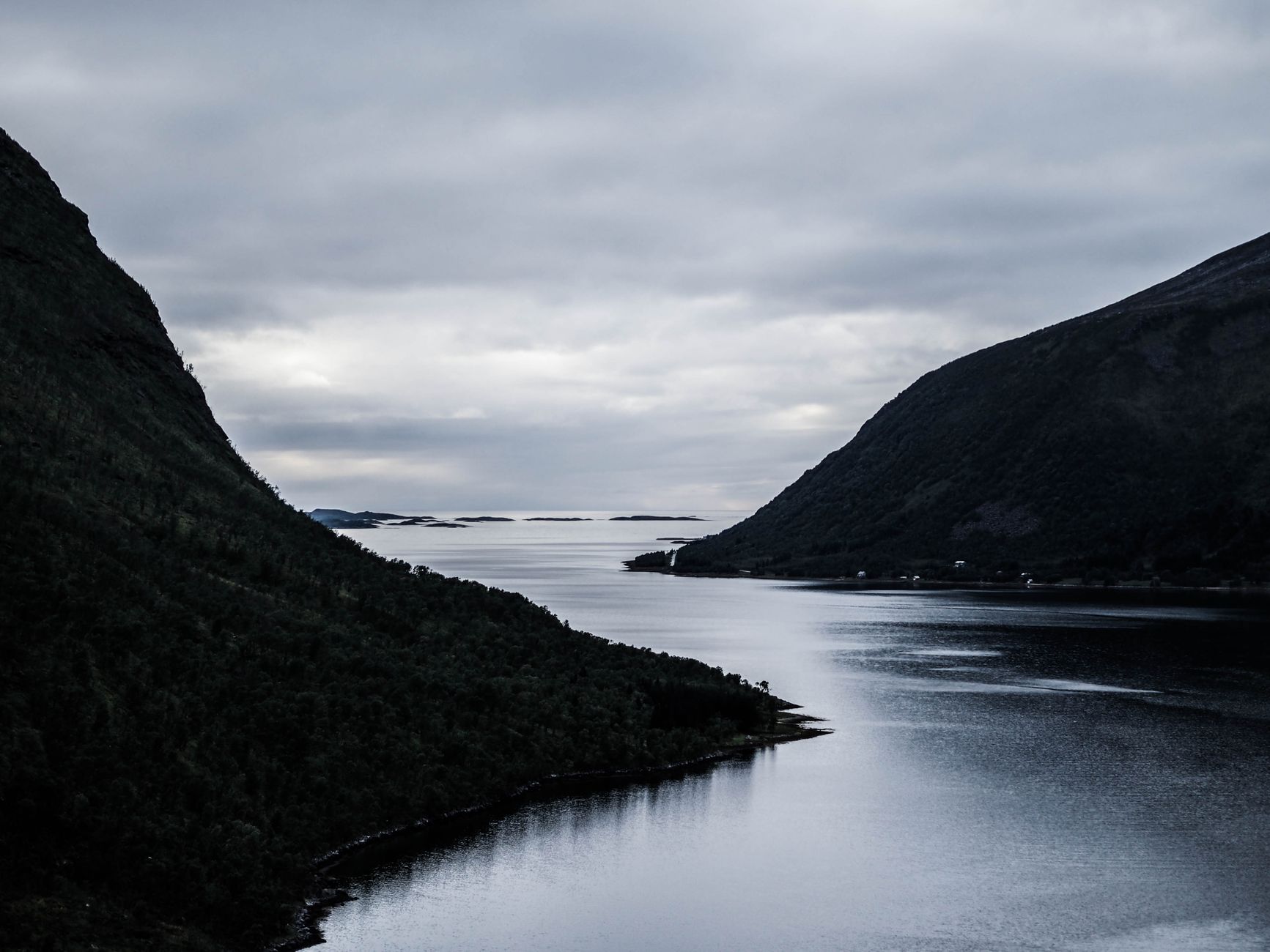 A Norwegian fjord stretching between layered mountains under dramatic cloud formations, capturing the scenic waterway cruise passengers experience departing Bergen.