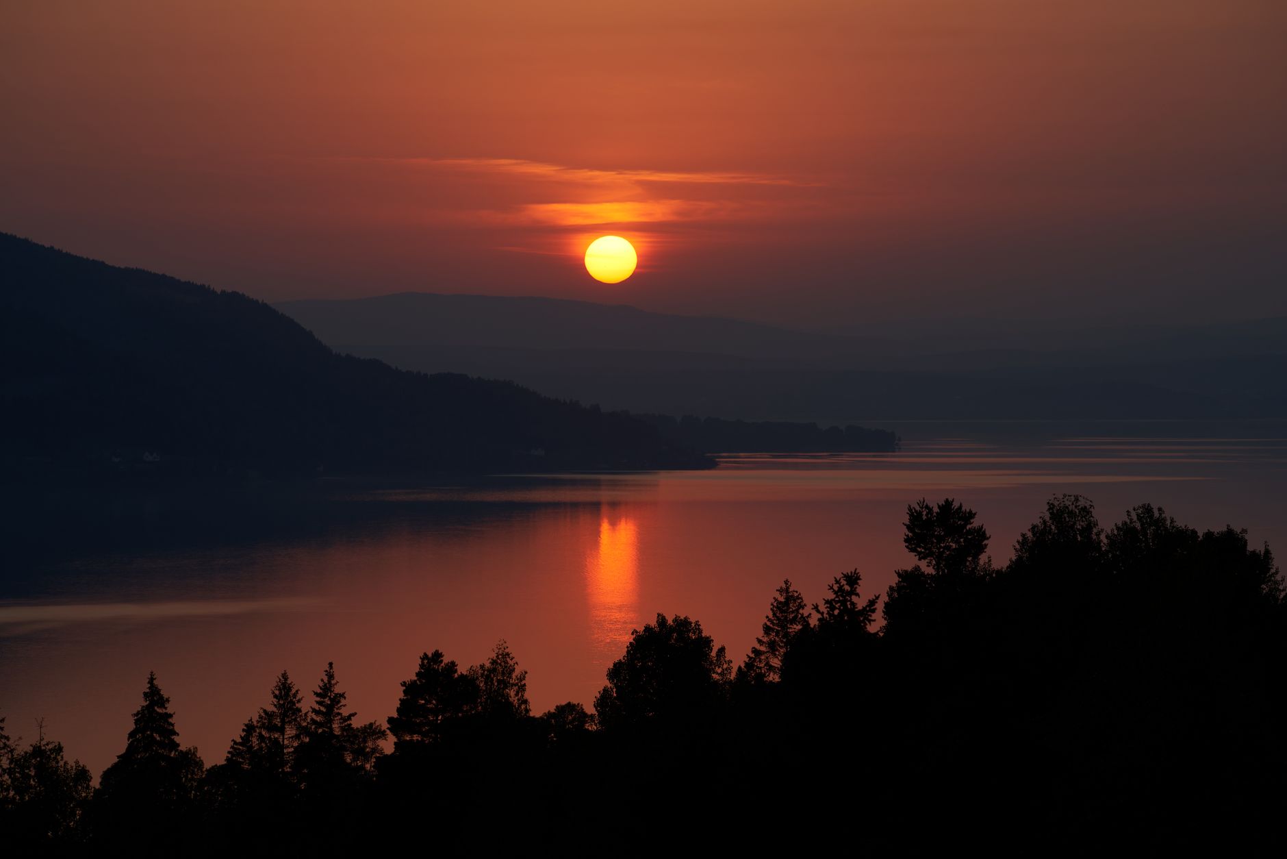 Golden sunset light reflecting across the calm, mirror-like waters of Tyrifjorden in Norway, illustrating the extended golden-hour conditions that define summer cruising seasons in Scandinavian fjords.