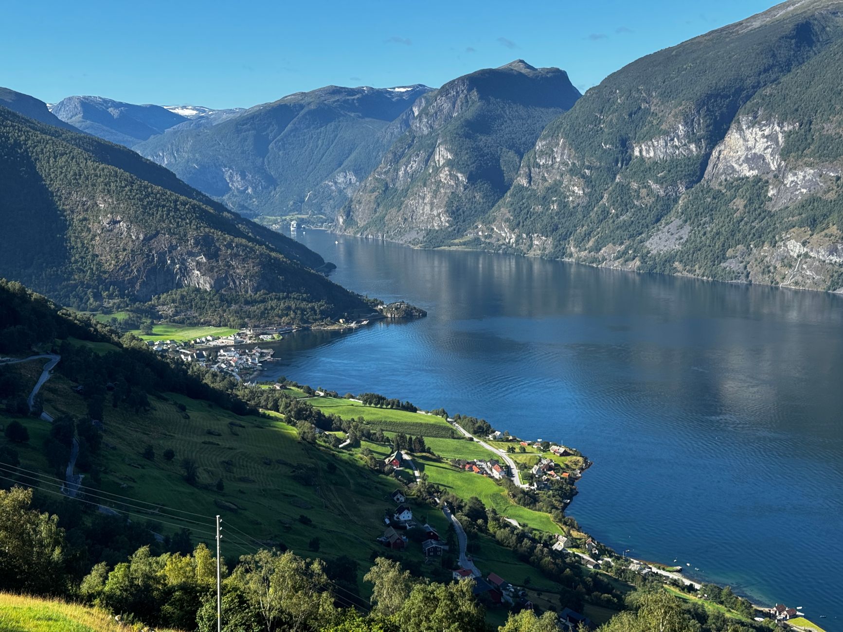 A sweeping view down a Norwegian fjord corridor flanked by steep, lush-green mountainsides — the kind of dramatic narrow passage cruise passengers encounter in fjord country.