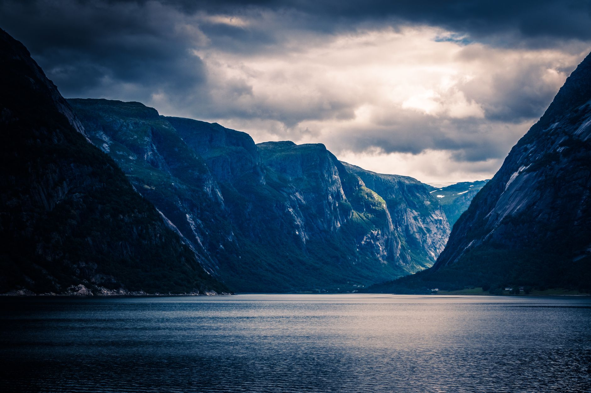A dramatic Norwegian fjord corridor flanked by towering cliffs, with serene, mirror-still water reflecting the moody sky above — capturing the immersive depth of a deep fjord passage.