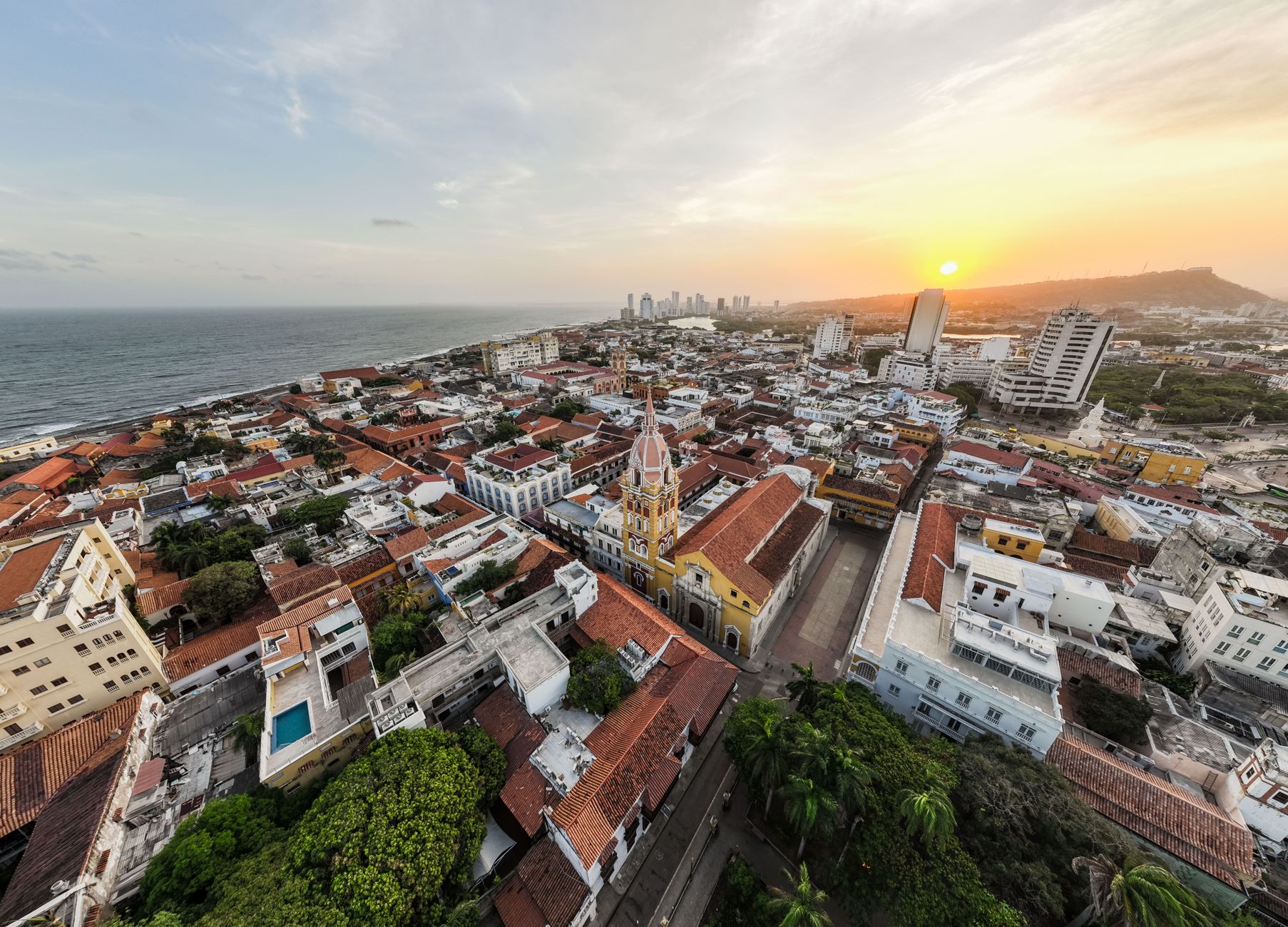 Aerial view of Cartagena's historic Old Town district at sunset, showcasing vibrant colonial architecture, terracotta rooftops, and historic domes against the Caribbean Sea.