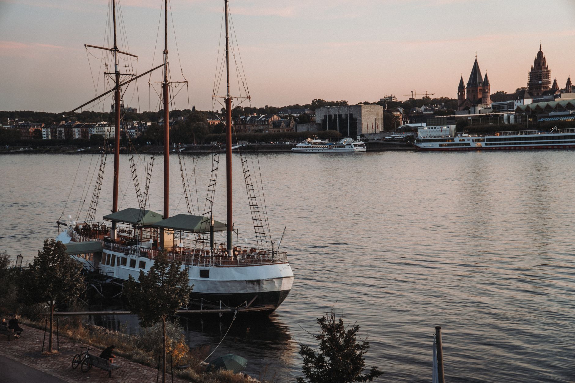 A moored ship glowing with warm evening light in a tranquil harbor at dusk, evoking the intimate twilight atmosphere aboard a boutique river cruise vessel.