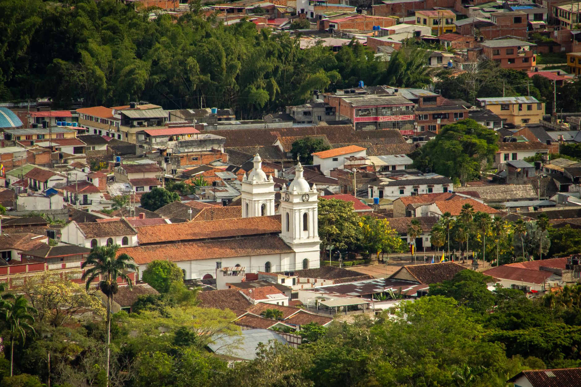 Aerial view of the Colombian town of Salento featuring a historic church surrounded by colorful colonial rooftops and lush green hillsides, evoking the cultural heritage of Colombia's riverside and mountain communities.