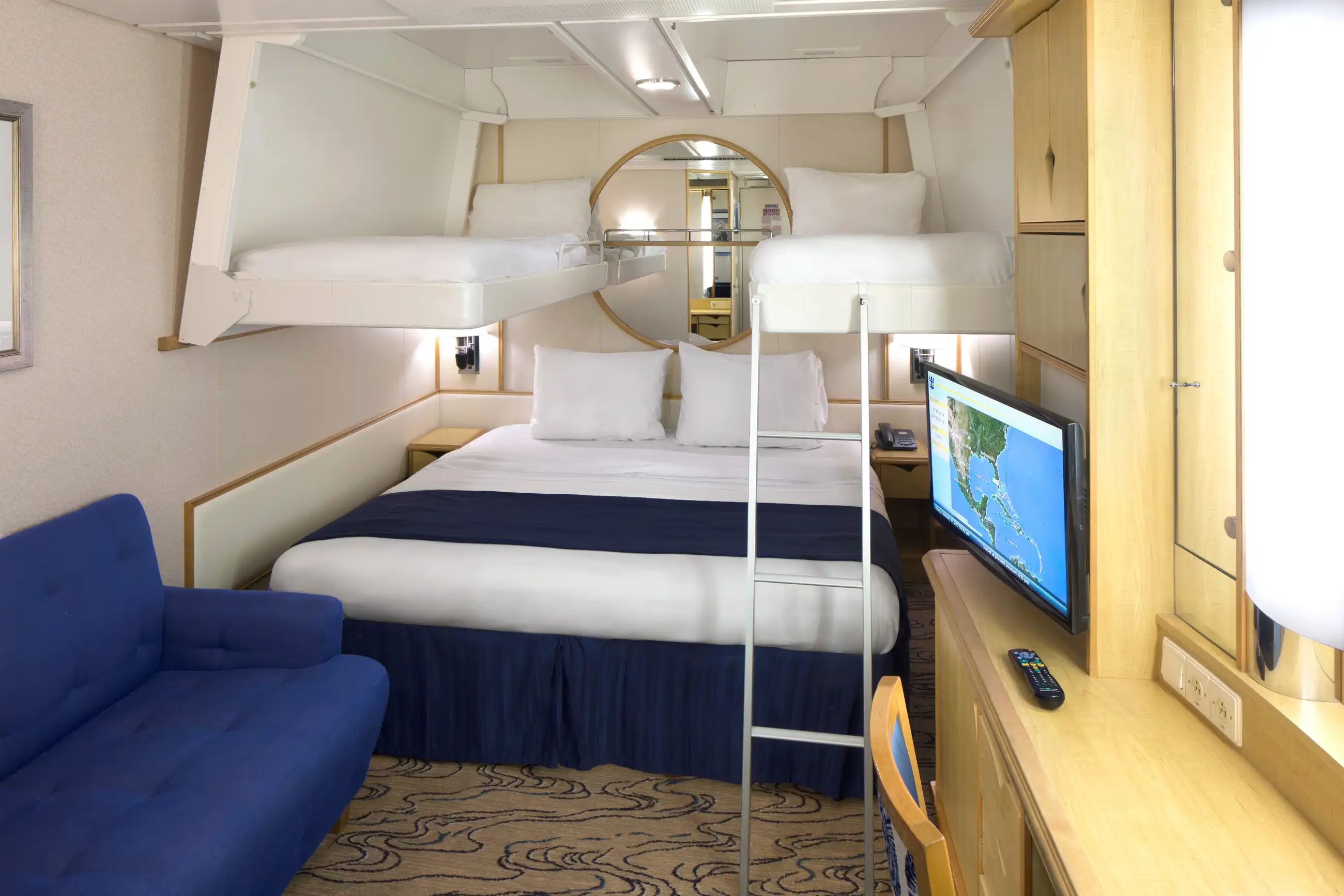 A compact interior stateroom on Navigator of the Seas with bunk beds, navy bedding, a small blue sofa and built-in storage.