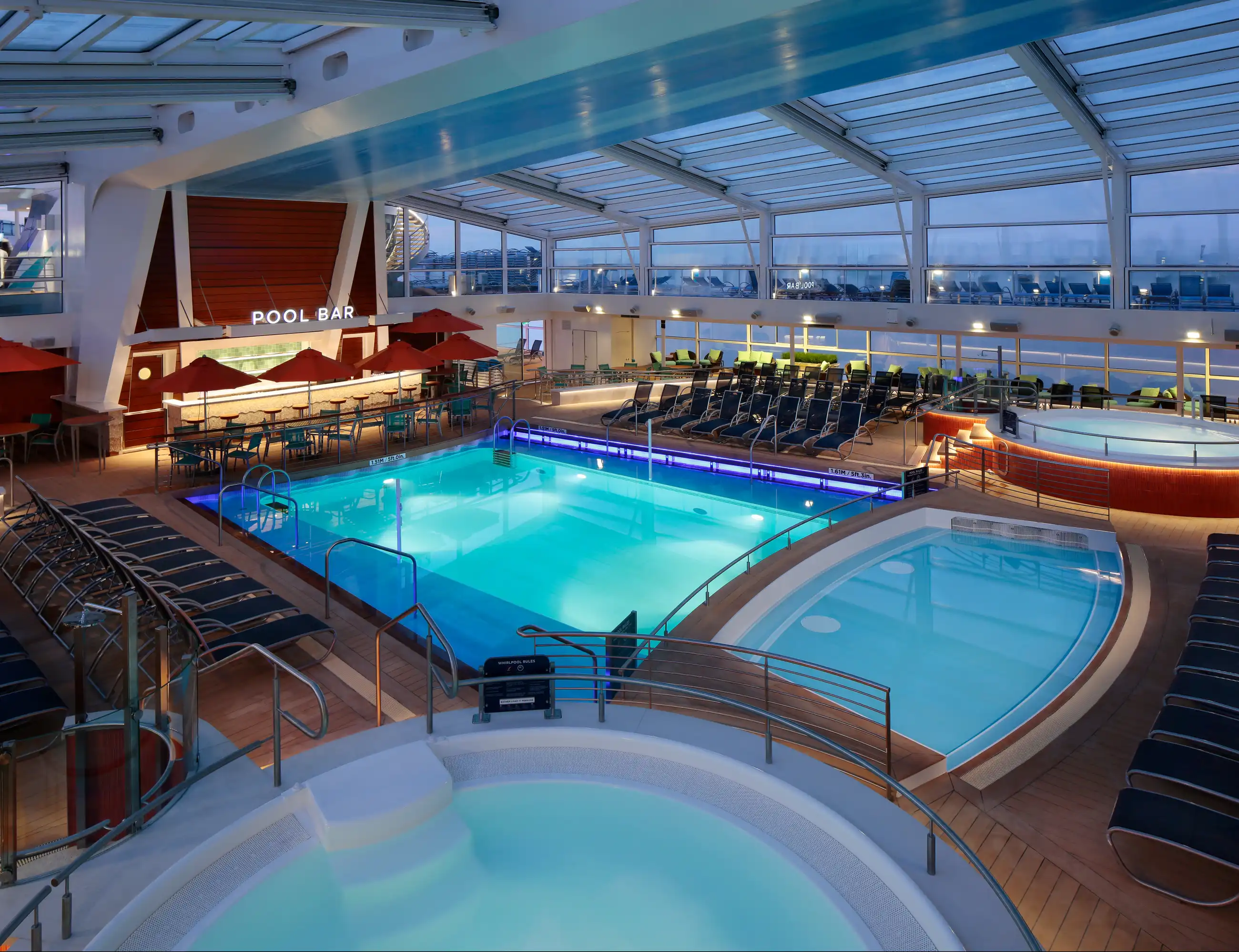 The glass-roofed Solarium pool deck on Quantum of the Seas, with a large turquoise indoor pool, hot tub and pool bar under panoramic windows.