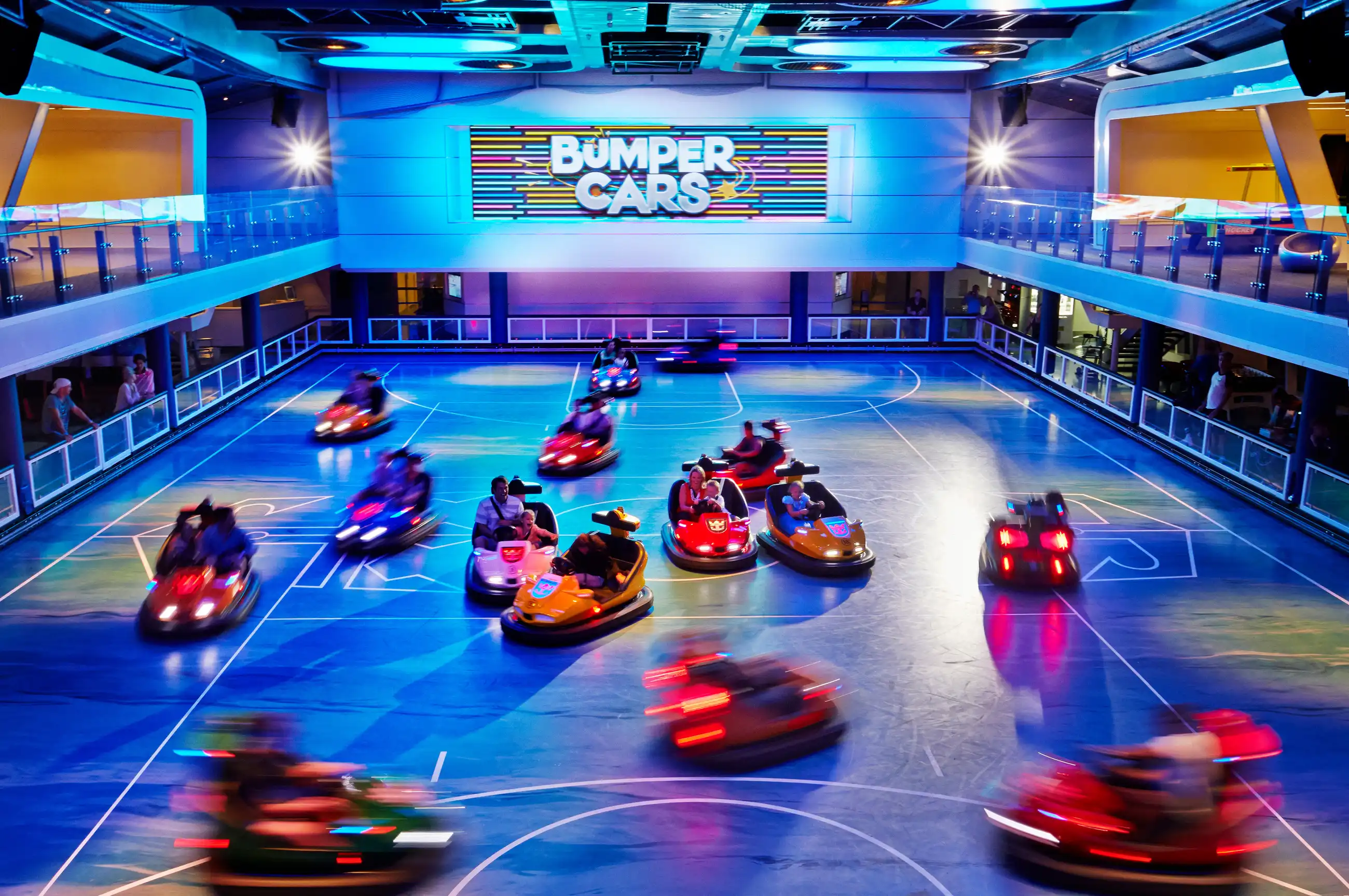 Guests of all ages drive neon-lit bumper cars in the indoor arena on Quantum of the Seas while spectators watch from above.