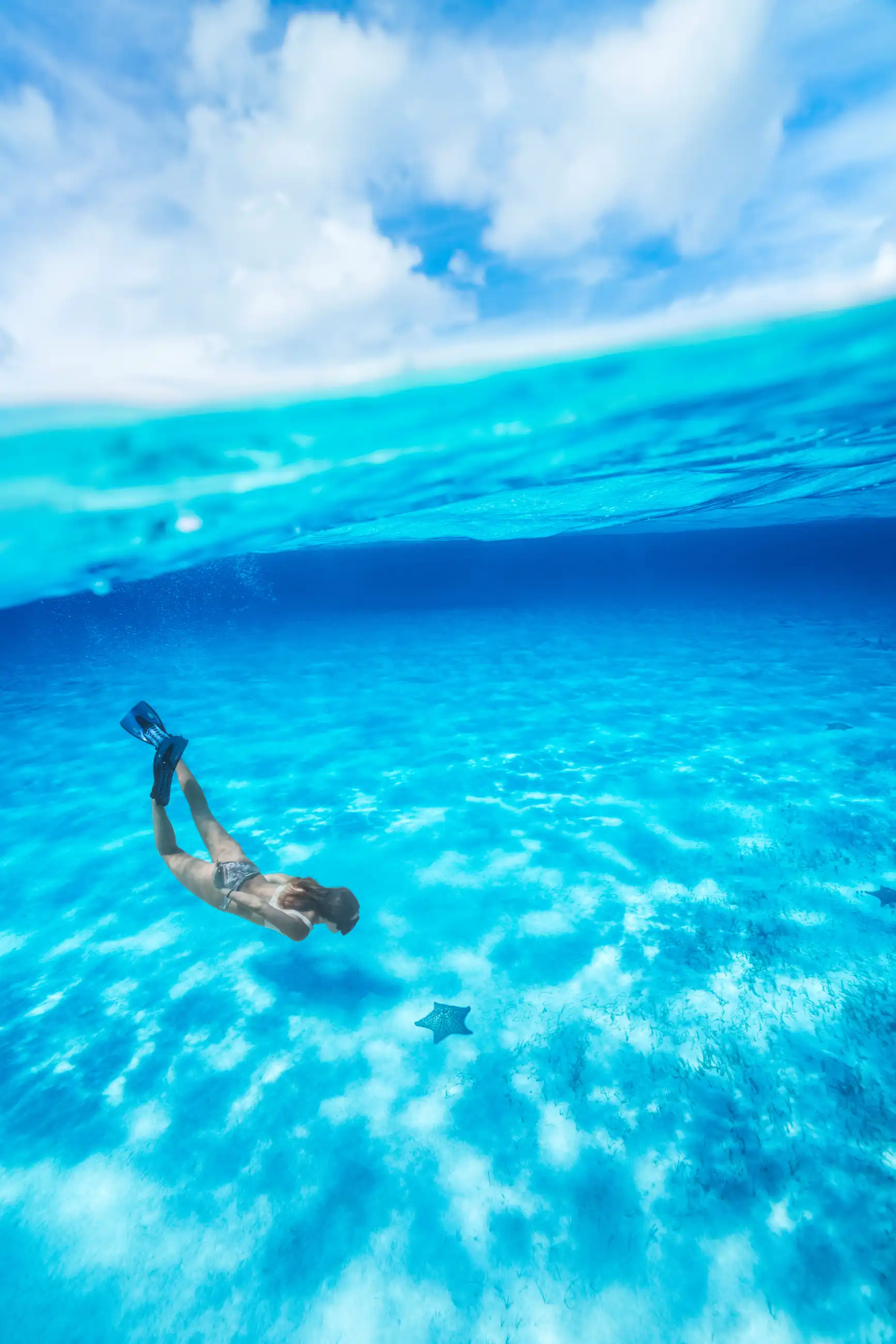 Split-level shot of a snorkeler gliding through clear turquoise water off Cozumel, Mexico, with blue sky above the waterline.