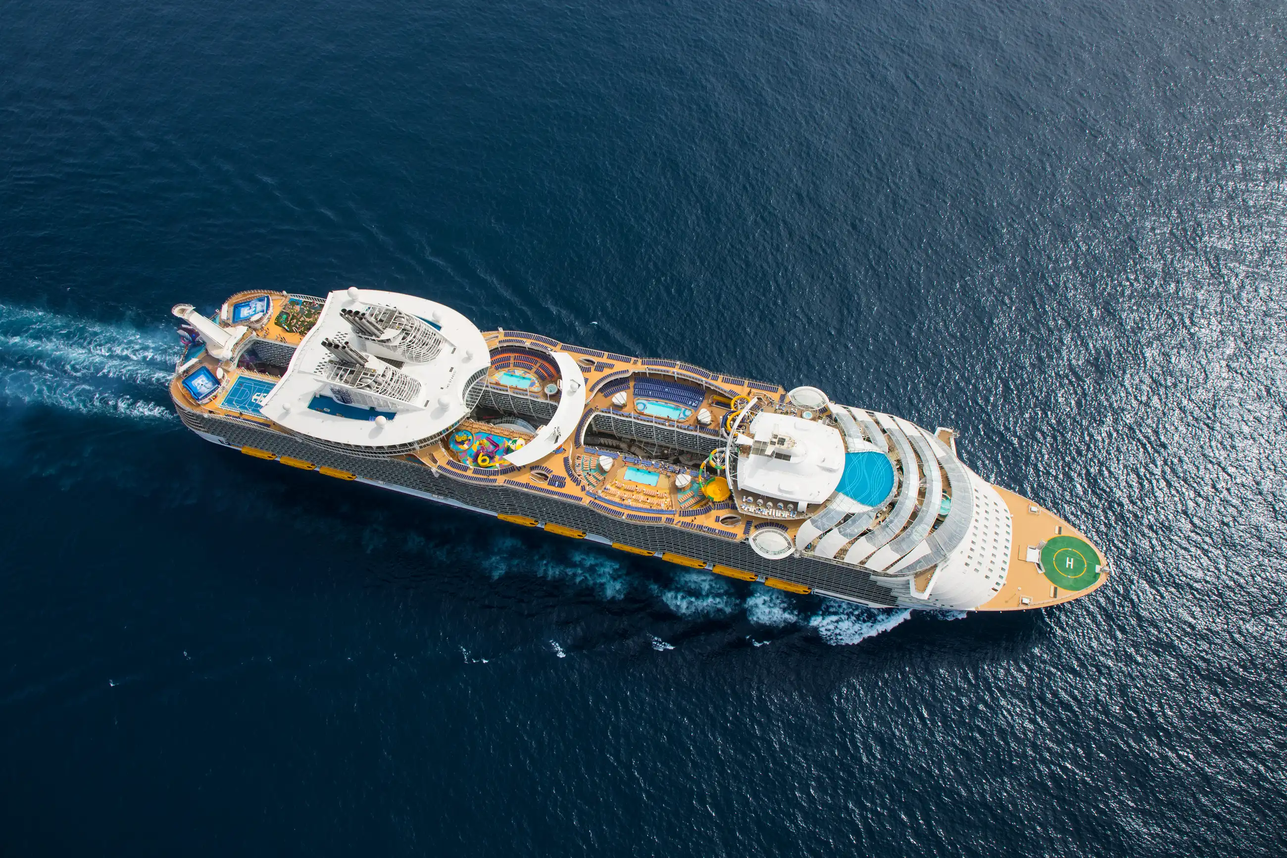 Overhead aerial of Royal Caribbean's Symphony of the Seas crossing deep blue open ocean, wake trailing behind the hull.