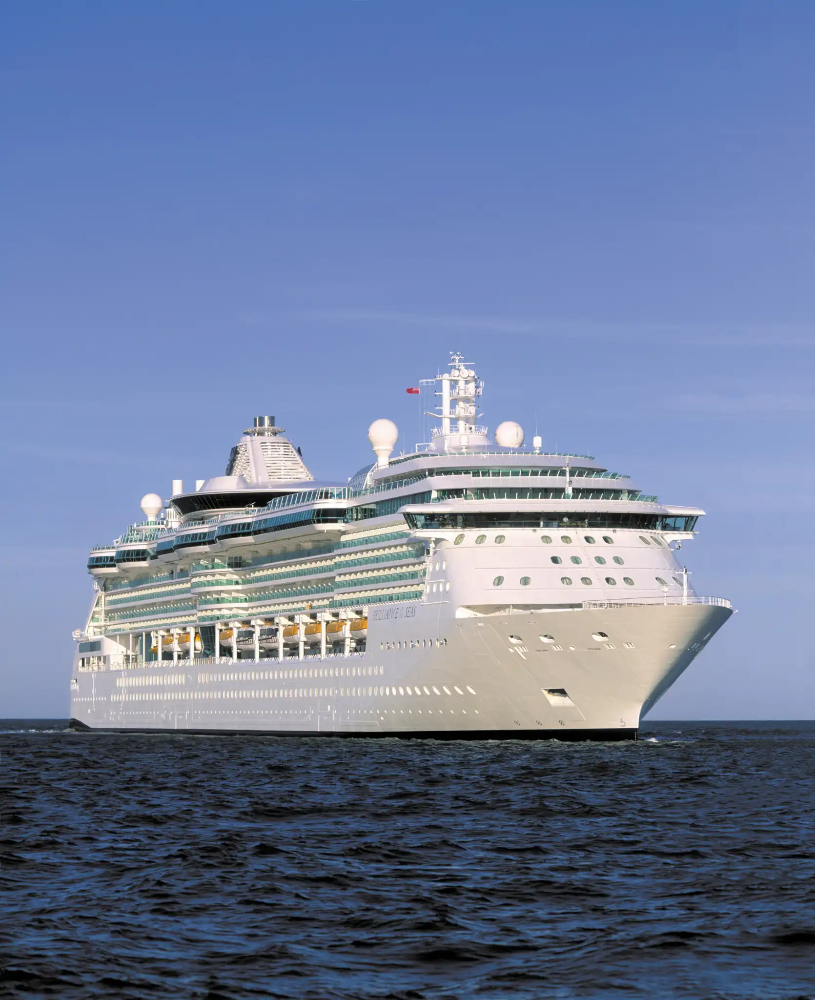 Starboard profile of Royal Caribbean's Brilliance of the Seas at sea, showing her tiered balconies and turquoise-trimmed white hull under clear skies.