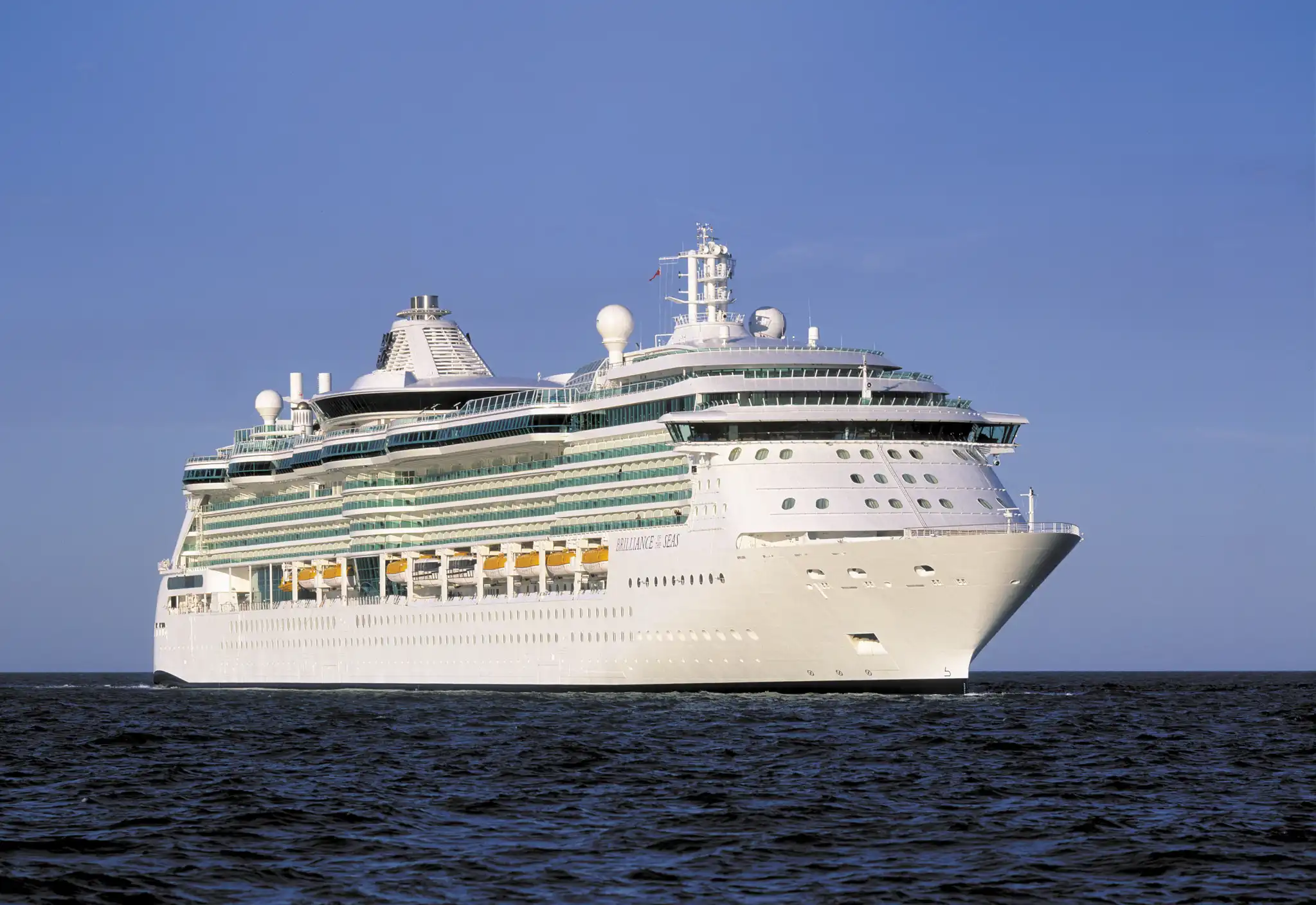 Brilliance of the Seas photographed from the starboard side on calm water, her multi-deck white hull marked with a horizontal green-blue stripe.