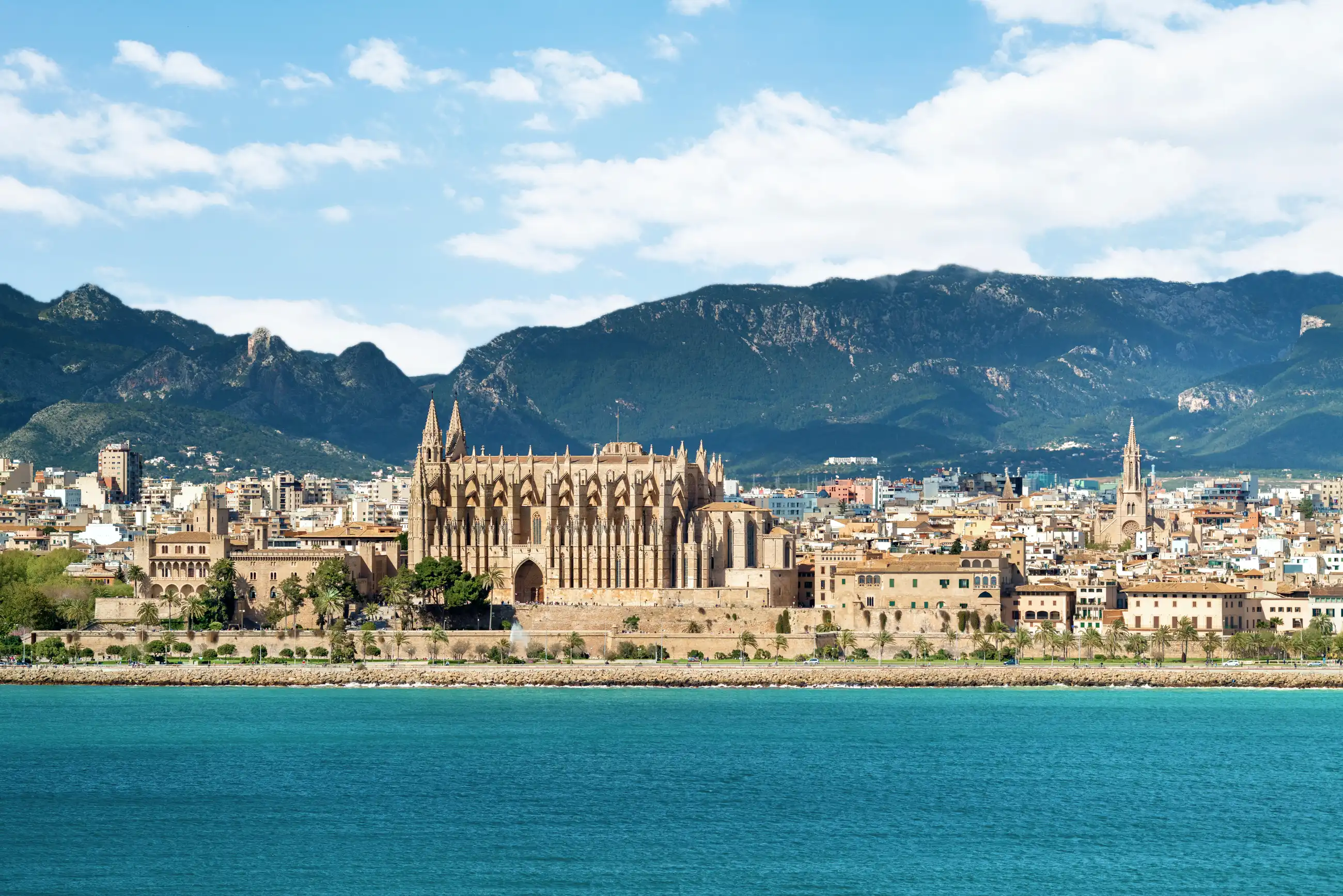Palma de Mallorca Cathedral (La Seu) seen from the Mediterranean, its Gothic façade and flying buttresses rising above the Balearic waterfront with mountains behind.