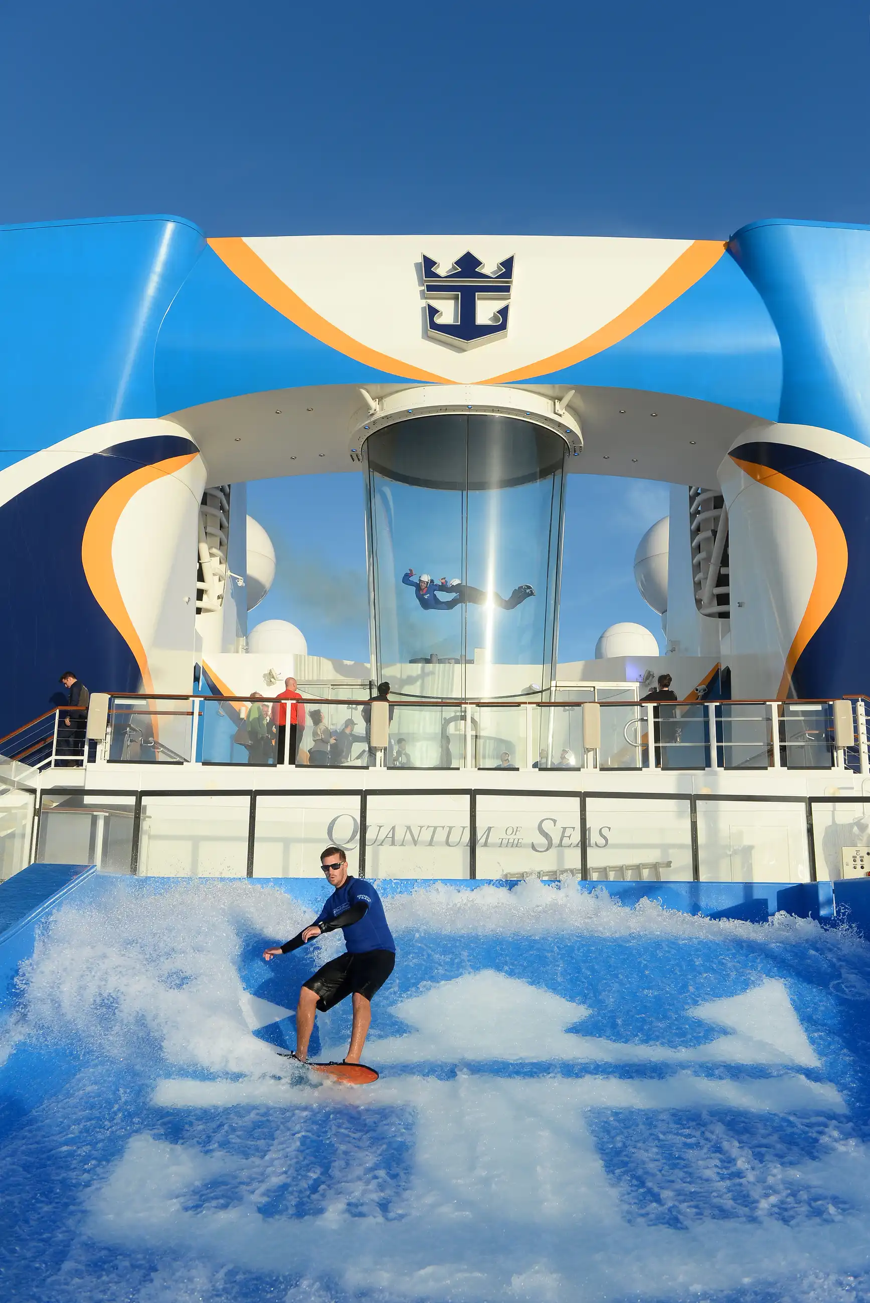 A surfer riding the FlowRider wave on Quantum of the Seas, with the ship's blue funnel and branding above the deck.