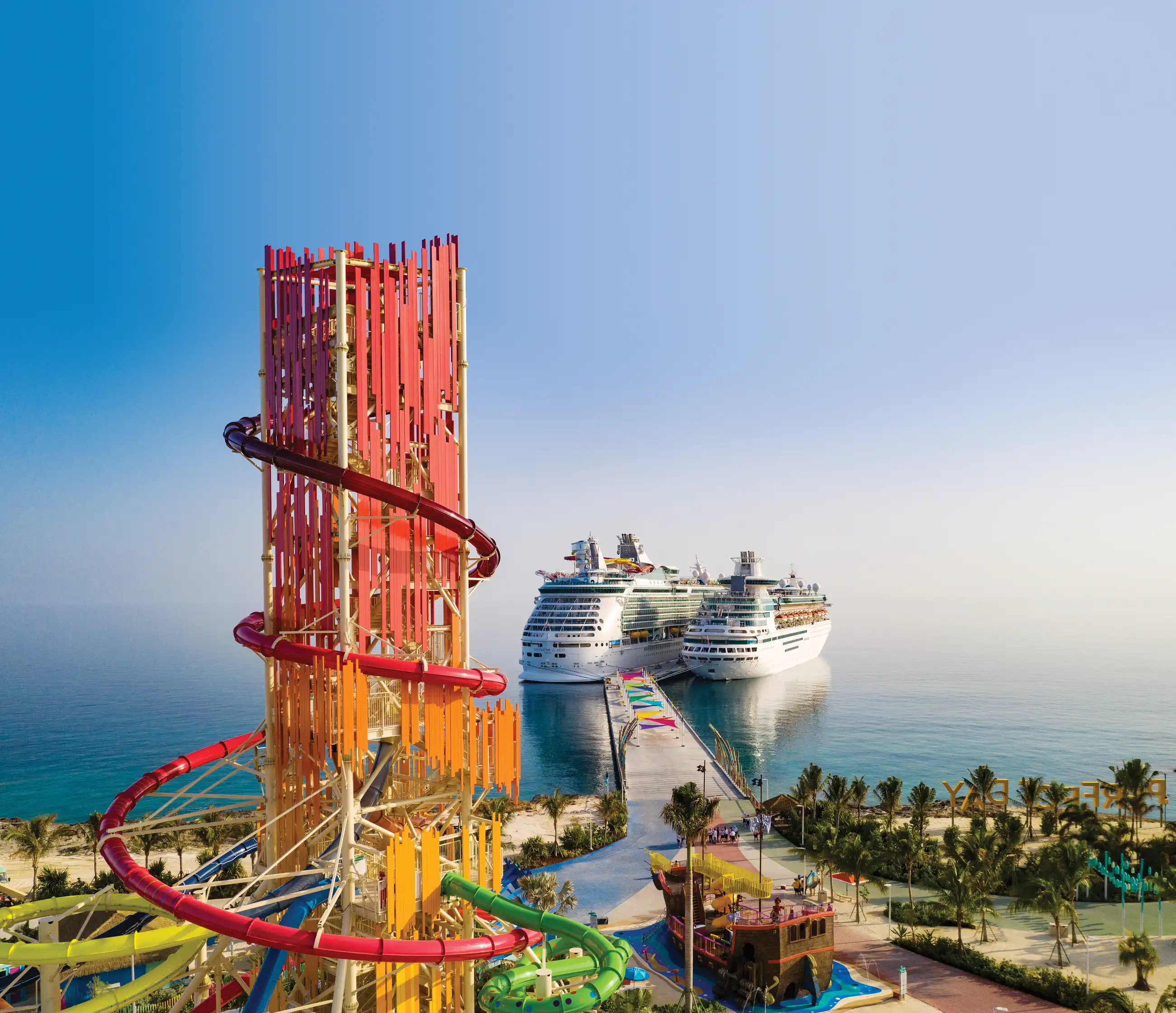 Navigator of the Seas docked behind the tall red-orange Daredevil's Tower waterslide at Royal Caribbean's private island destination.