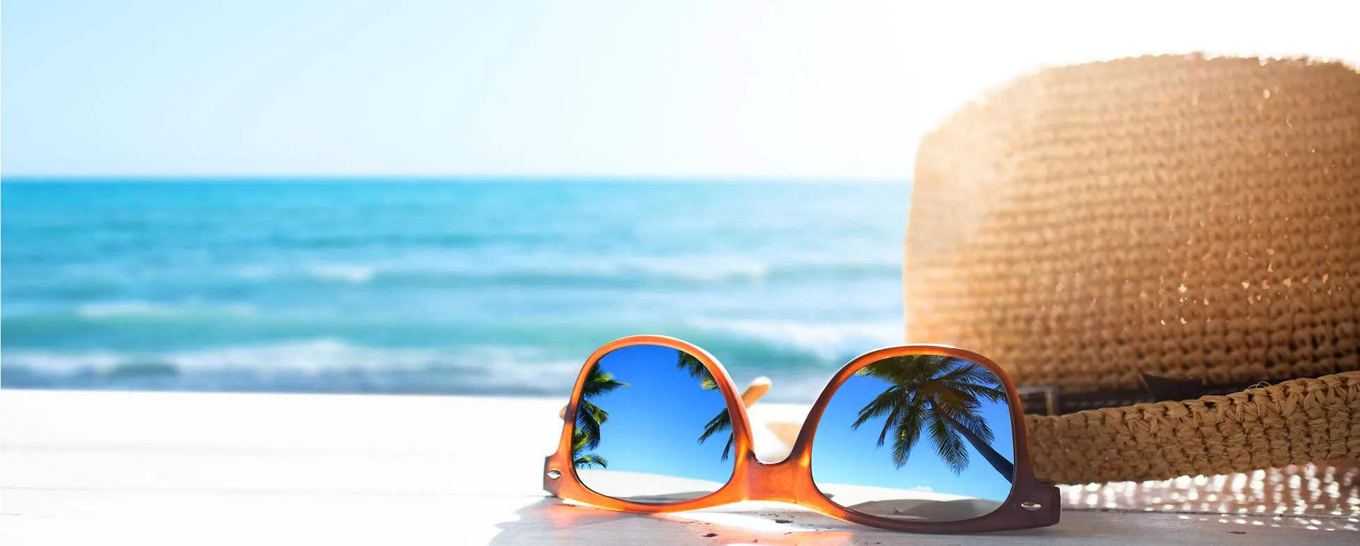 Sunglasses reflecting palm trees with straw hat by blue ocean waves