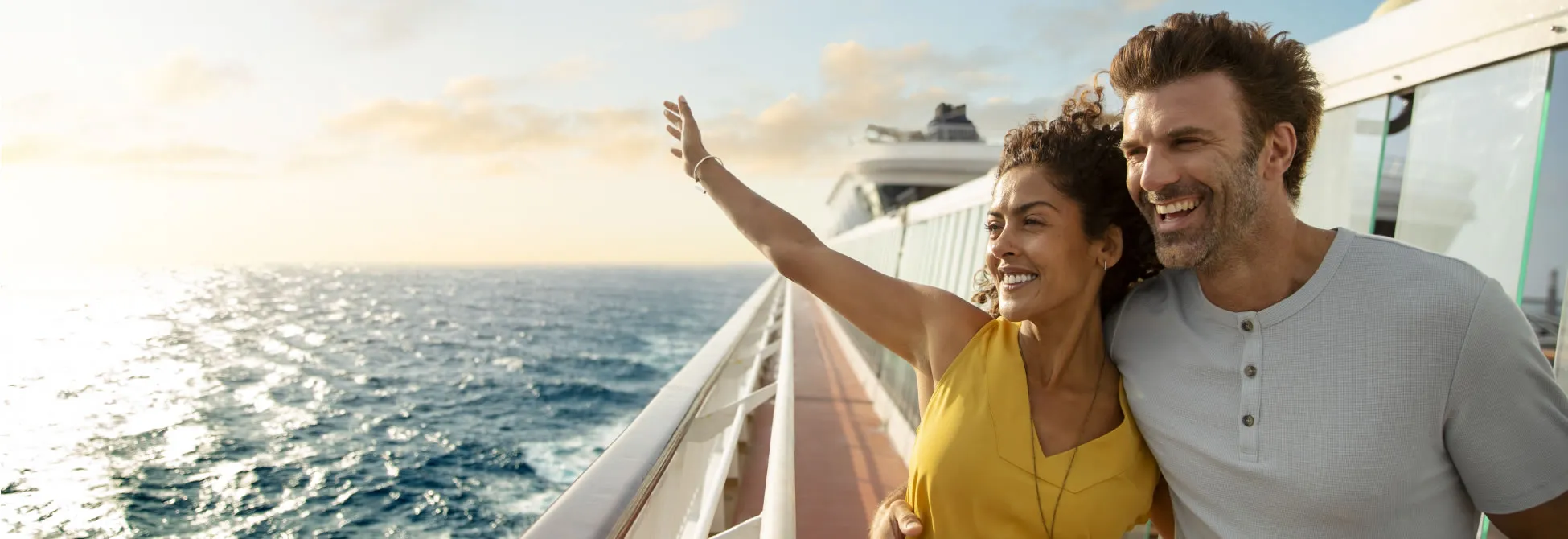 Couple enjoying cruise vacation, woman waves with ocean behind them
