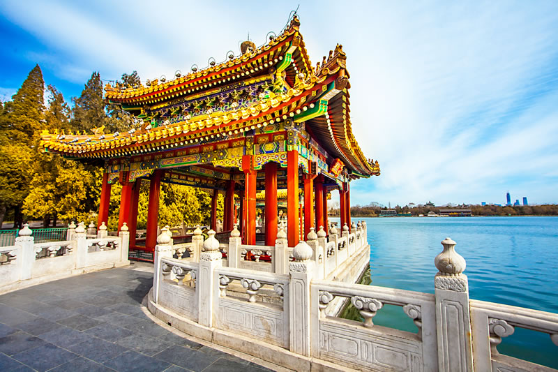 Ornate traditional Chinese pavilion by blue lake with autumn trees