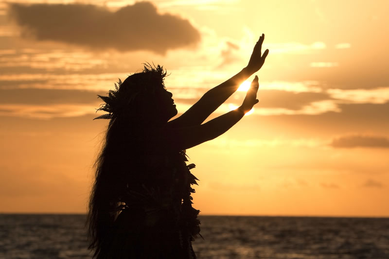 Silhouette of hula dancer raising hands during golden sunset by ocean