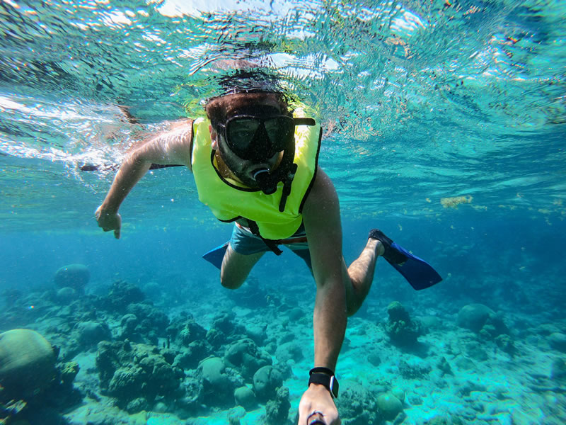 Snorkeler in bright yellow vest exploring vibrant underwater coral reef