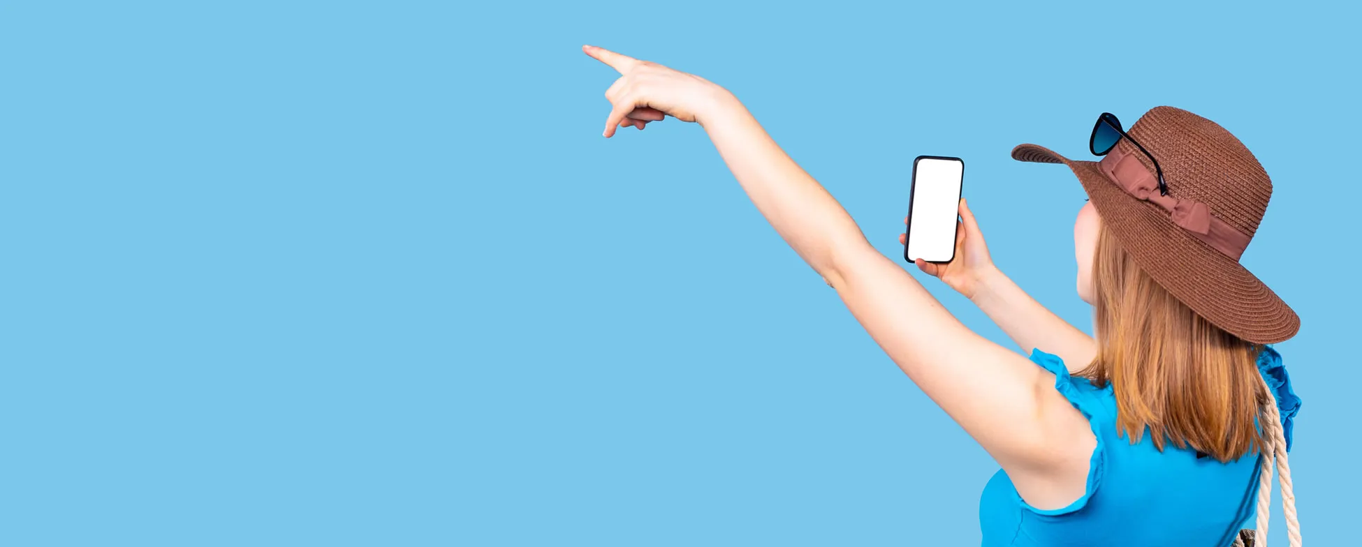 Person in blue shirt and sun hat pointing while holding smartphone