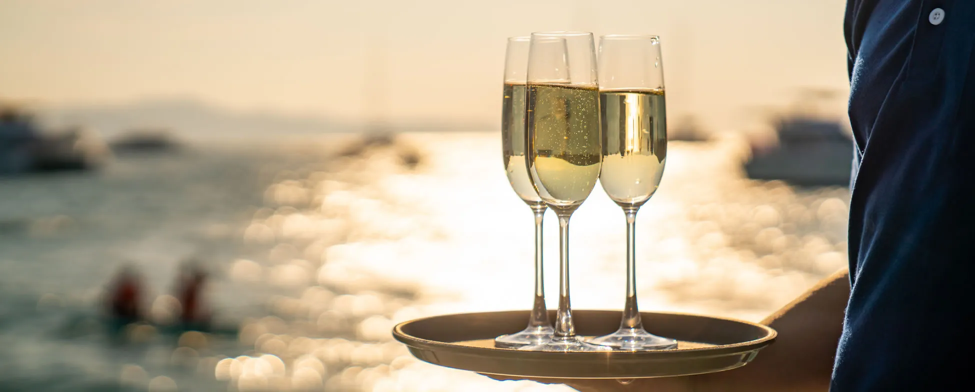 Three champagne flutes on a tray with blurred ocean background