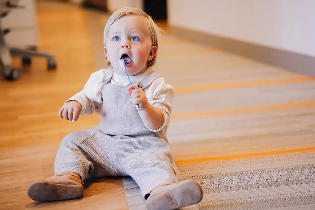 Baby sitting on the floor holding a toothbrush