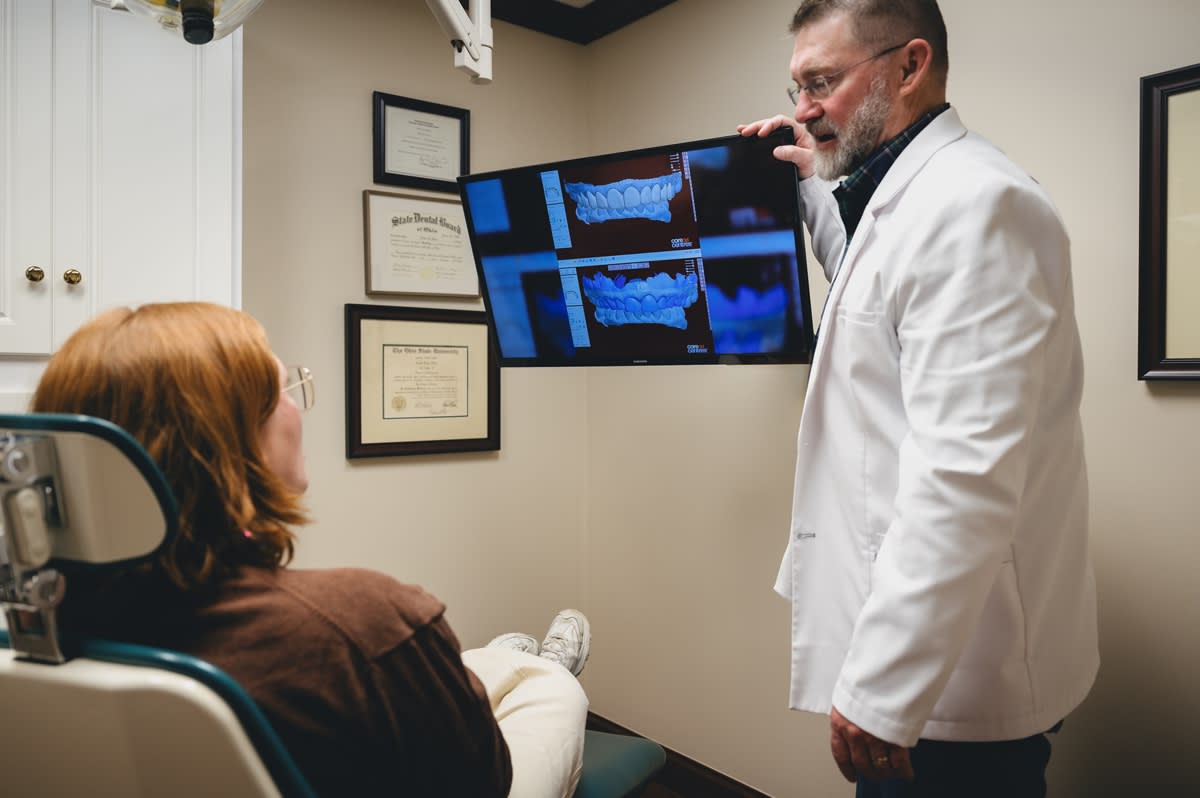 Dentist pointing to dental imaging on monitor while discussing treatment plan with patient