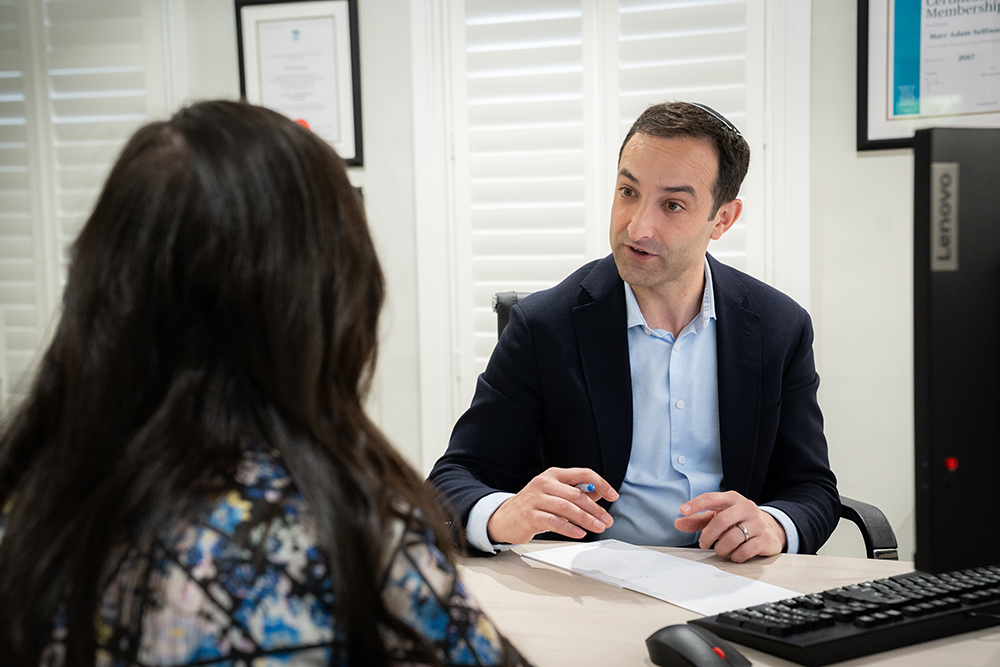Woman sitting at desk discussing before and after of plastic surgery with doctor. images of breast augmentation on computer screen beside them.