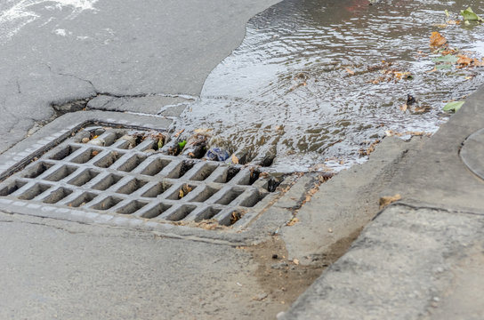 Water drains into a storm drain on the road close-up Photos | Adobe Stock