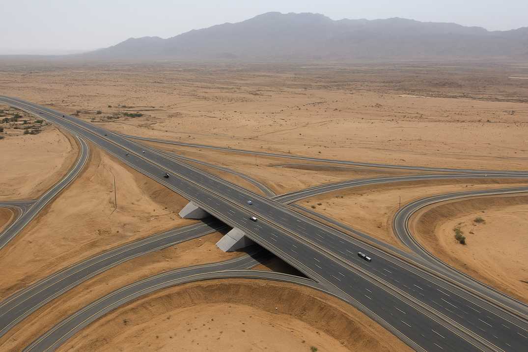 High-resolution aerial view of a desert highway interchange in Saudi Arabia with overpasses and curved ramps.