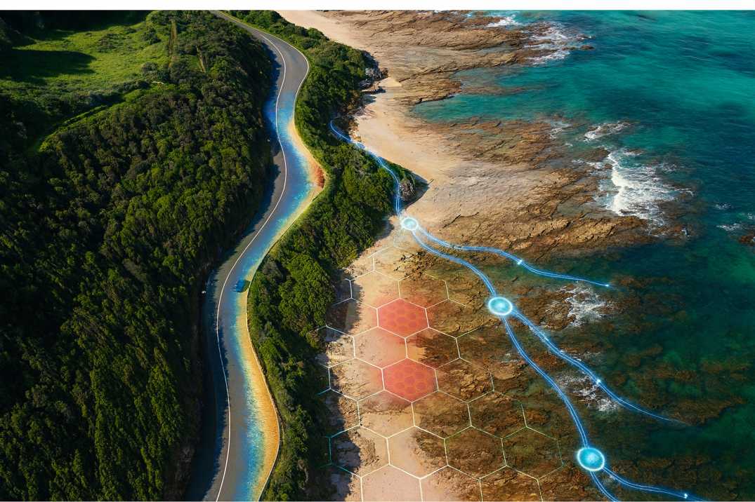 A winding coastal road beside green cliffs and turquoise water, viewed from above.
