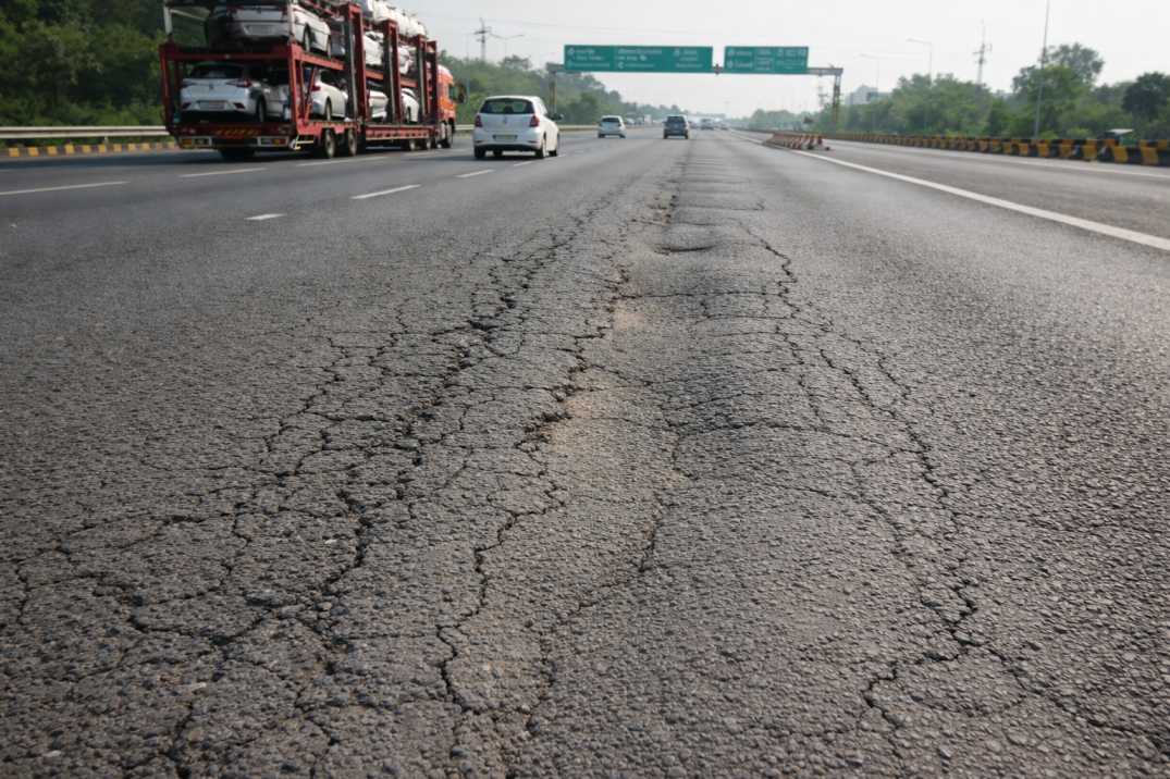 Indian highway pavement with early-stage cracking and rutting under traffic in daylight