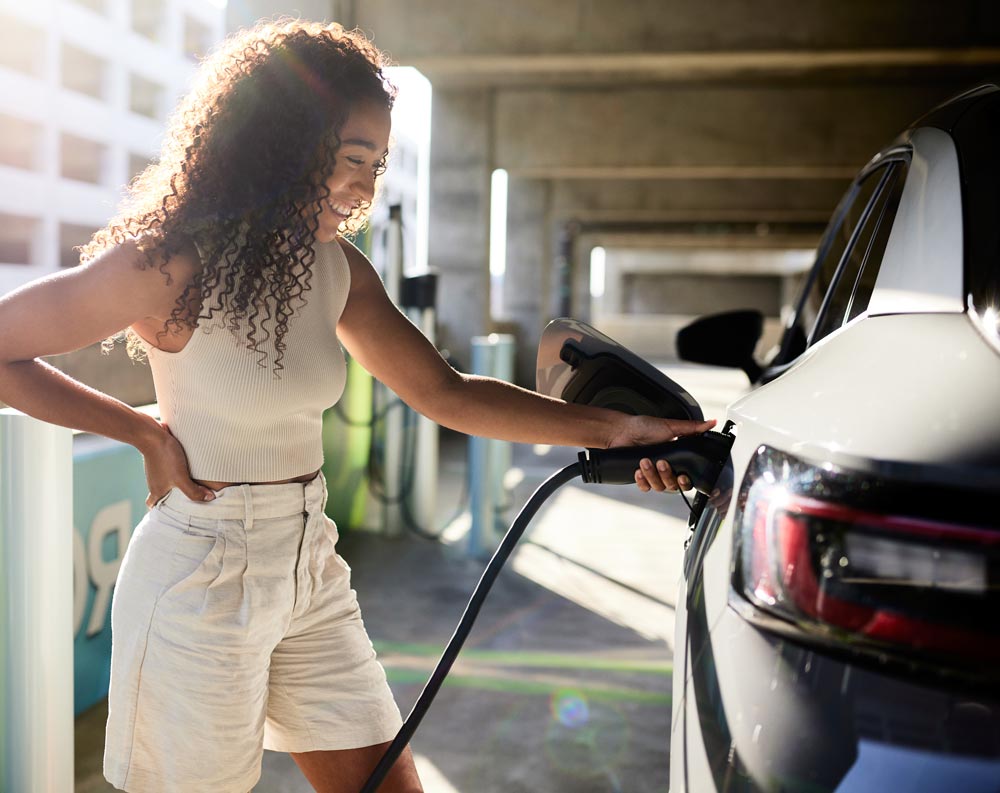 A woman is seen charging her electric car at a charging station, highlighting the shift towards electric vehicles.