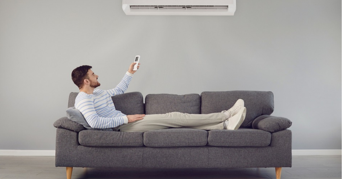 Barbat fericit pe canapea folosind aparatul de aer conditionat