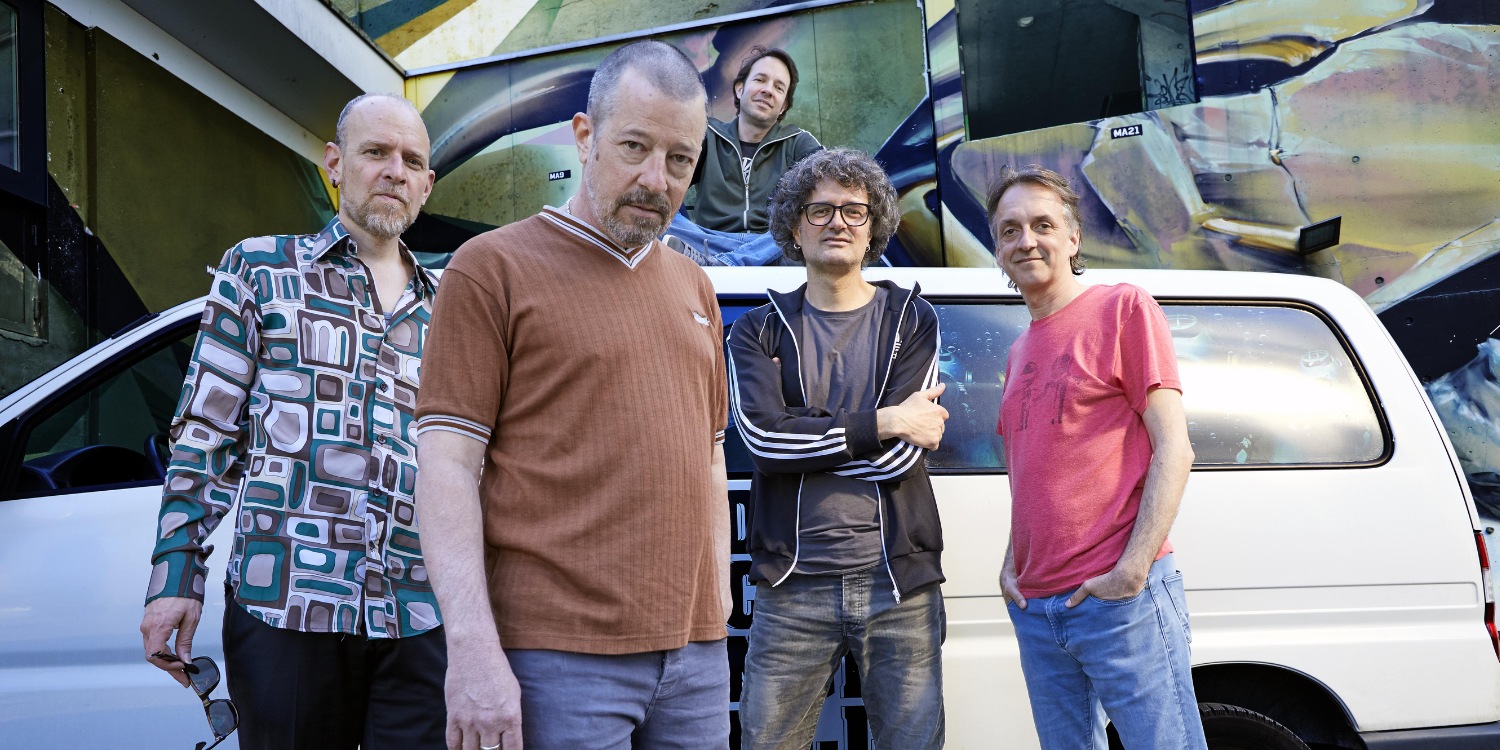 Die Band posierend vor einem Auto.