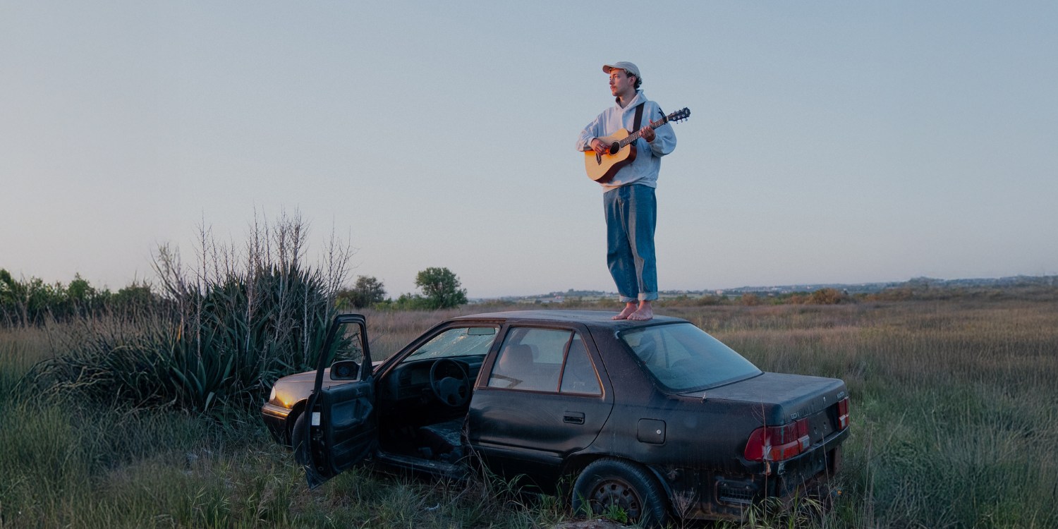 Sinu mit Gitarre, barfußstehend auf einem alten Auto. Mitten in der Natur.