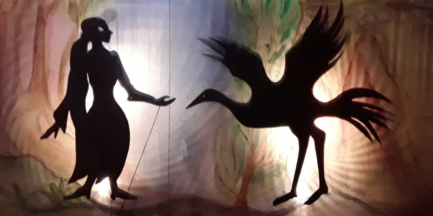 Die Schatten von einem Mädchen und einem Kranich vor einer Leinwand mit Waldbild.