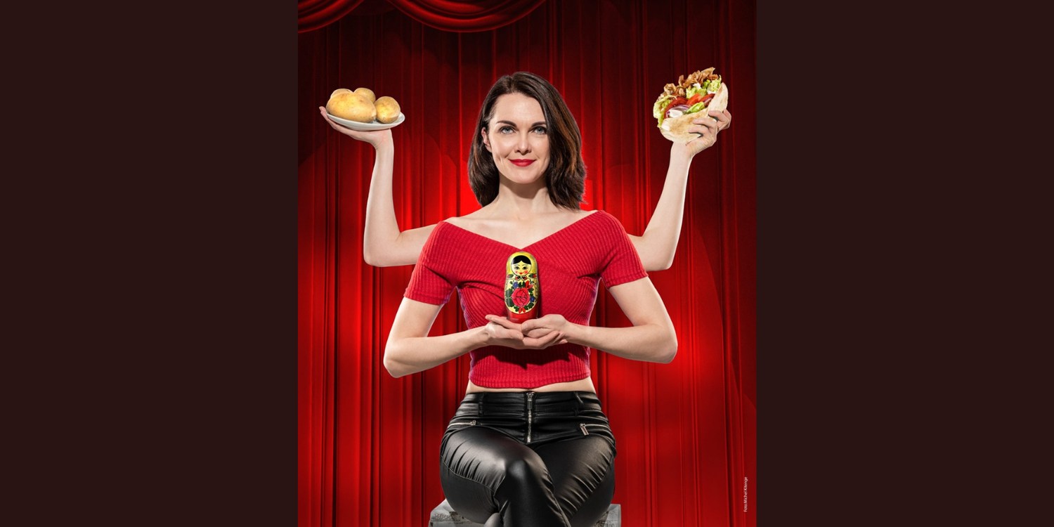 Liza Kos mit vier Armen, in denen sie Kartoffeln, Döner und eine Matrjoschka hält.