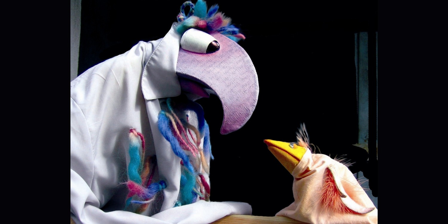 Zwei Thetaerpuppen. Ein großer lilafarbener Vogel und ein kleiner Gelber sitzen sich gegenüber.