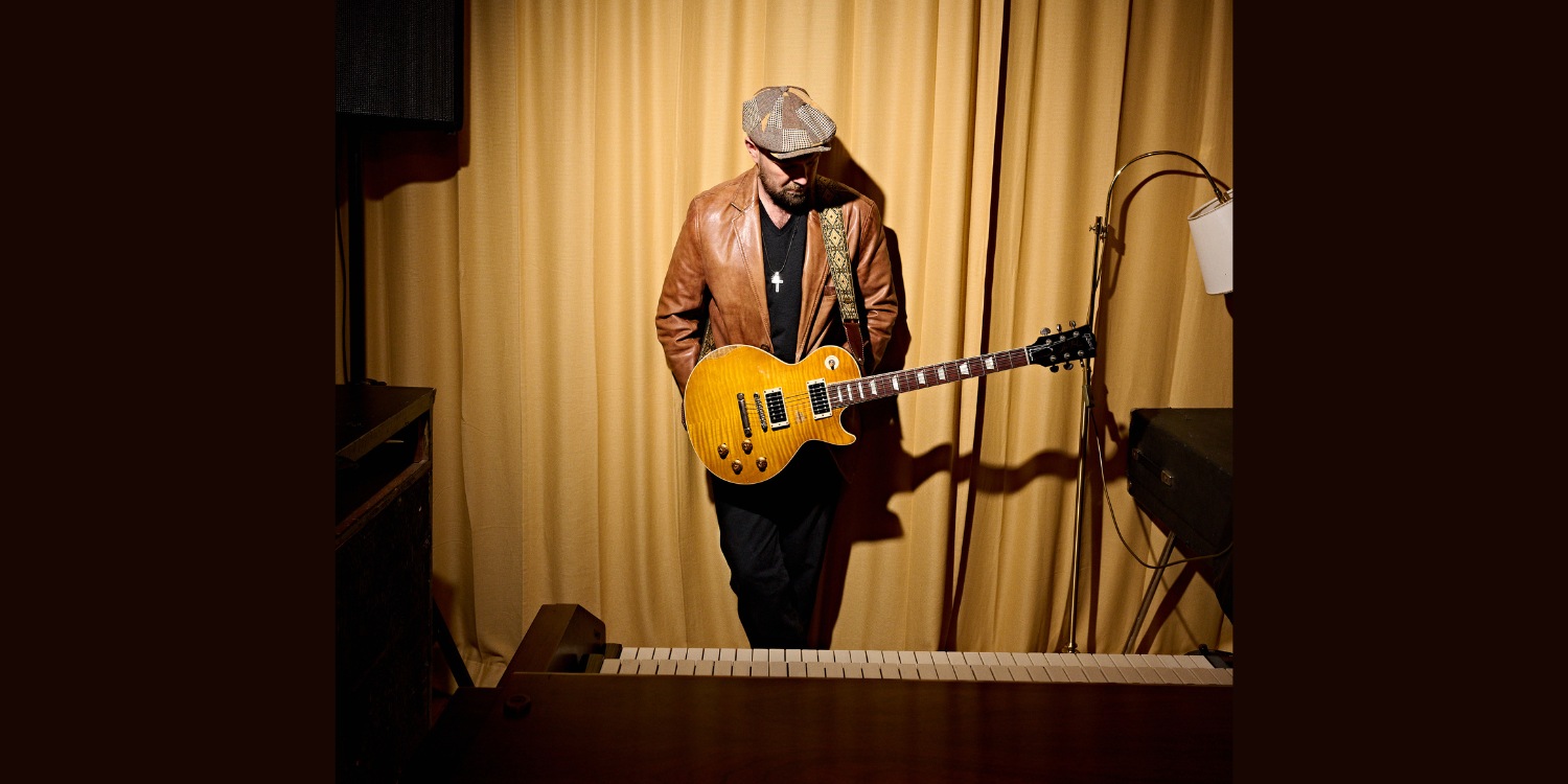 Henrik Freischlader mit umhängender Gitarre im Scheinwerferlicht stehend.