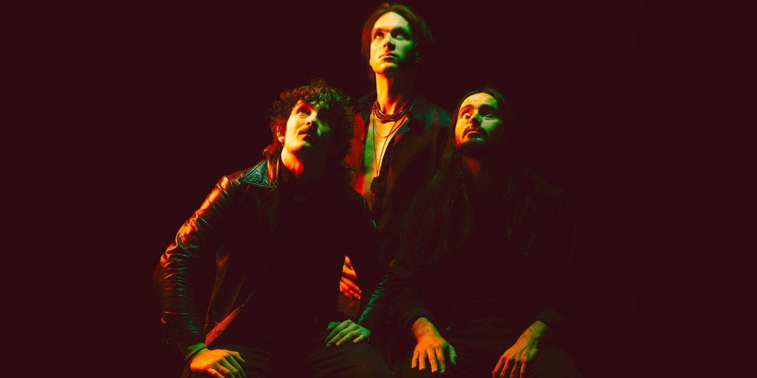 Die Band Dirty Sound Magnet im dunklen Raum. Alle Drei schauen nach oben.