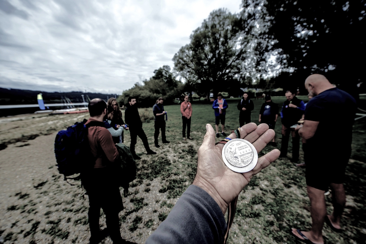 Group on the Lipno shore with a hand holding a medal in the foreground