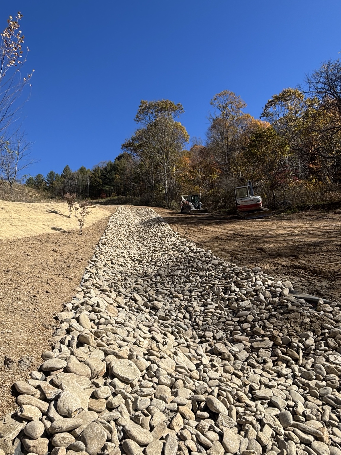 River-stone drainage channel beside graded and planted ground