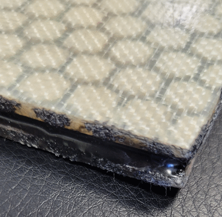Close-up of a textured honeycomb pattern sheet with adhesive on the edges on a black surface.