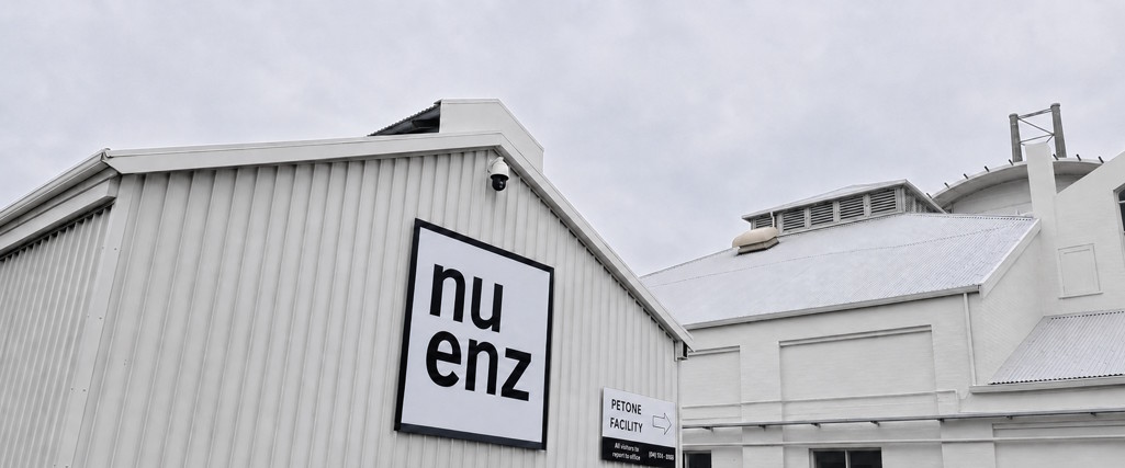Gray industrial building with a large sign displaying 'nuenz' on its wall under a cloudy sky.