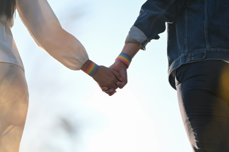 Two Black youth are holding hands wearing rainbow bracelets.