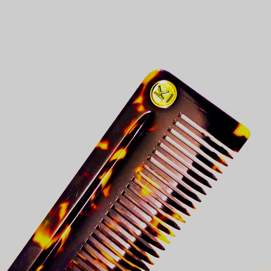 Close-up of a tortoiseshell patterned hair comb with a gold circular emblem on a gray background.