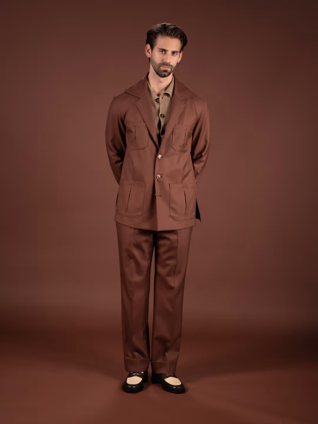 Mann mit braunem Anzug und beige-schwarzen Schuhen vor braunem Hintergrund.